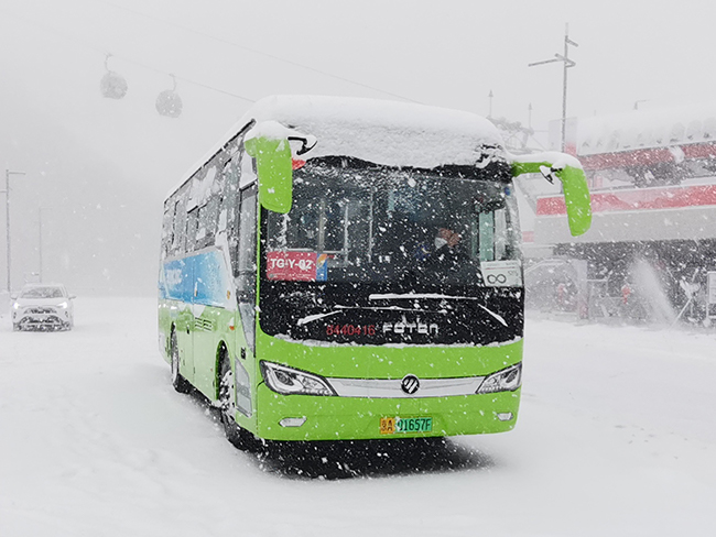 Green FOTON electric bus driving through heavy snow