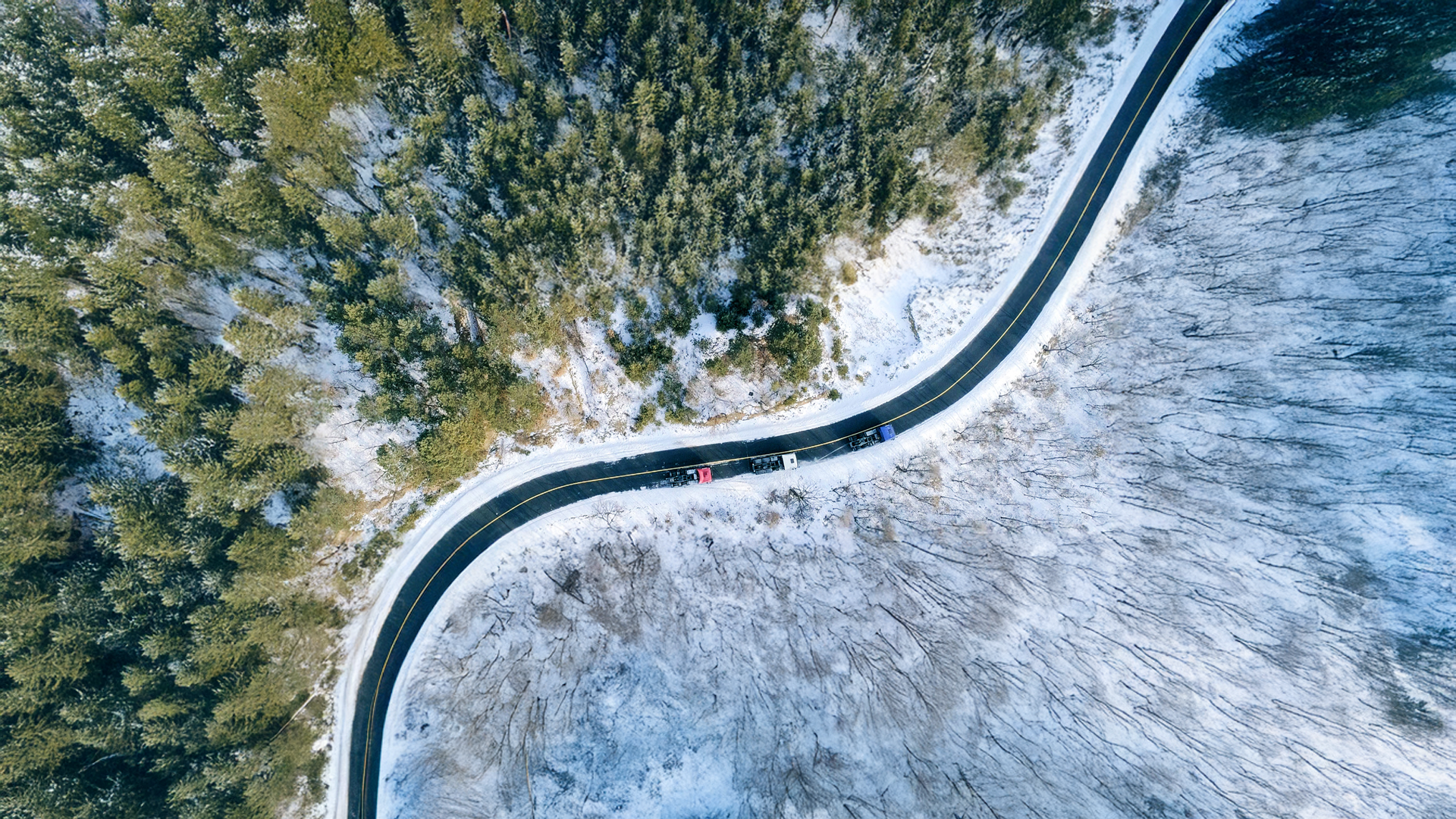 Aerial view of a winding road through a snowy forest